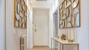 Un couloir avec une porte blanche, un radiateur et une console sur laquelle sont posées des bougies et une statue.