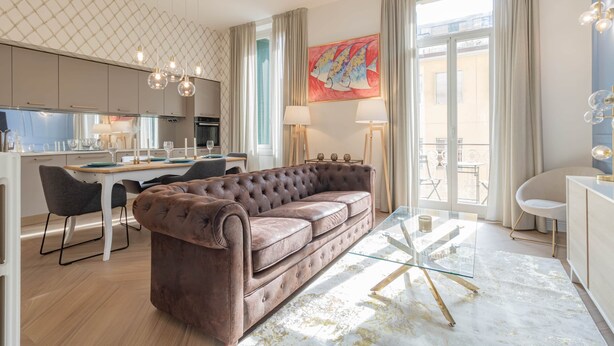 Un salon moderne avec un canapé capitonné, une table basse en verre et un coin repas comprenant une table et des chaises blanches.