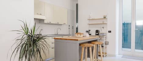A modern kitchen with a central island, bar stools, a potted plant, and a wall clock.