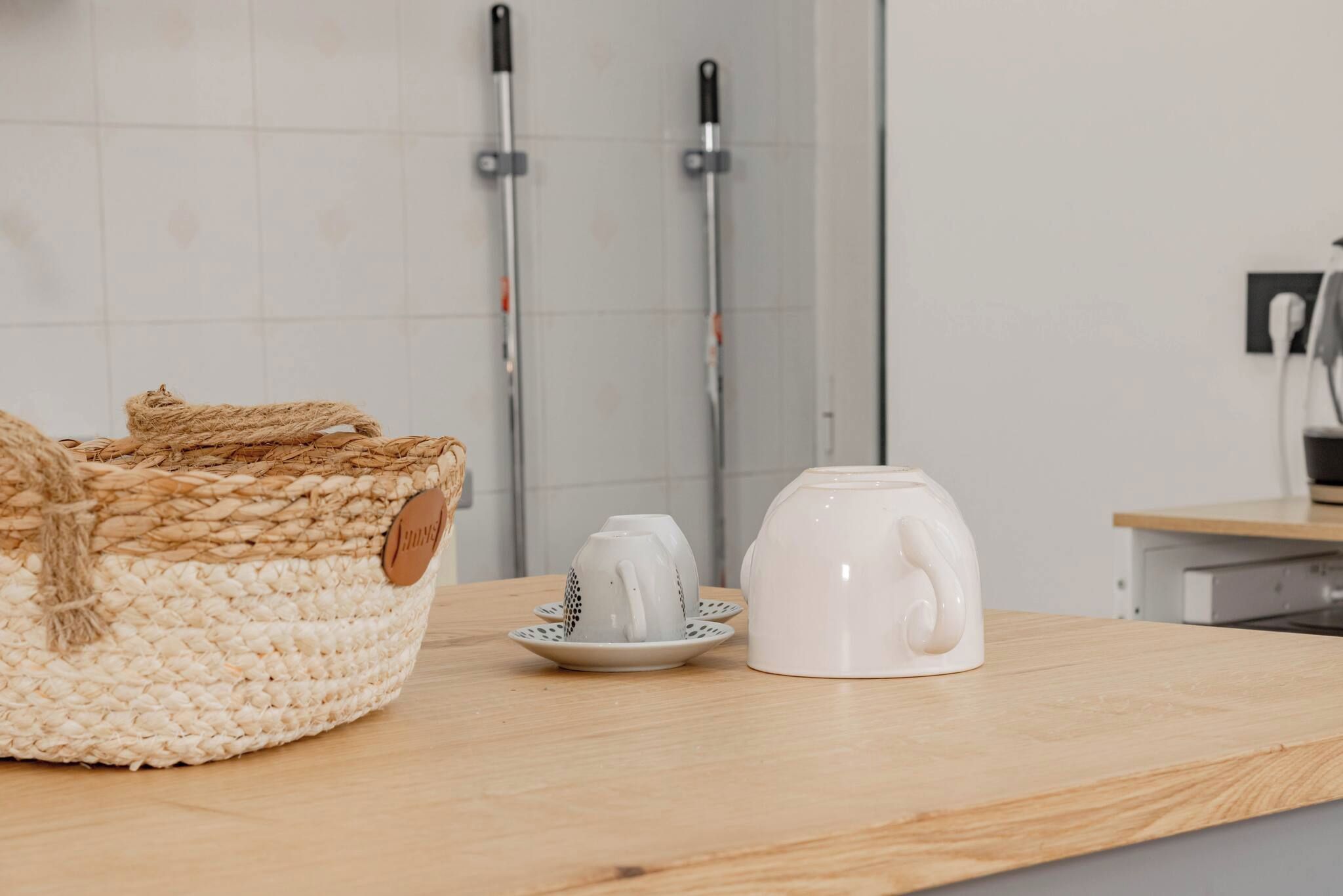 A kitchen counter with a woven basket, a white teapot, and a matching teacup on a wooden surface.