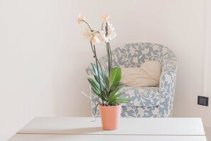 A potted orchid on a white table with a patterned armchair in the background.