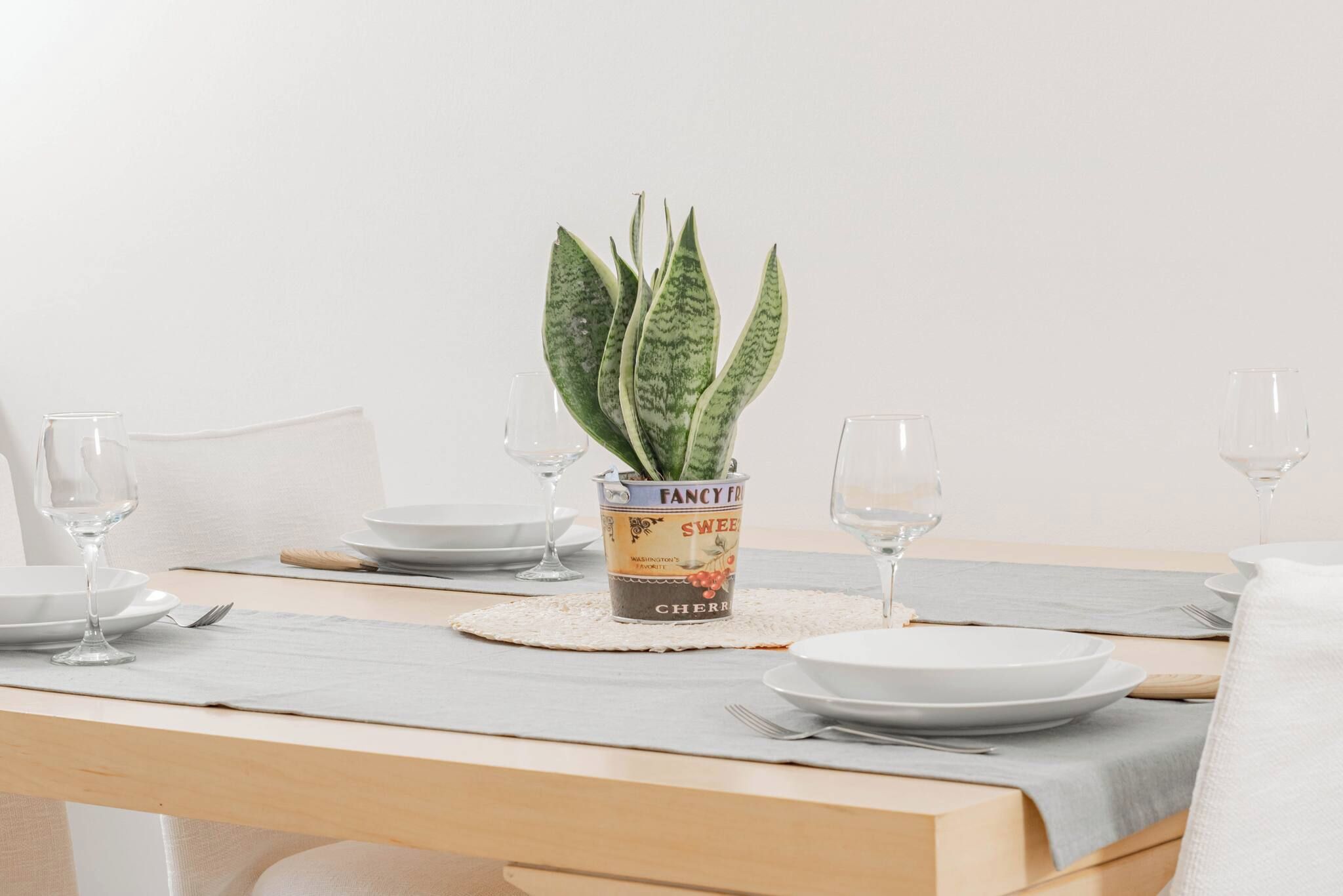 Una mesa de comedor dispuesta con platos, cubiertos y una planta decorativa en un recipiente de hojalata con el rótulo 'Fancy Free'.
