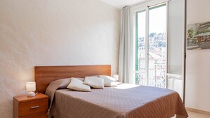 Una camera da letto con una testiera in legno, un letto con copriletto trapuntato, un comodino con una lampada e una finestra vista edifici.
