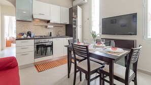 Una cucina moderna con mobili bianchi, un tavolo da pranzo per quattro persone e un televisore a schermo piatto montato a parete.