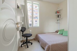 A bedroom with a bed, a desk, and a window.