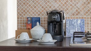 Un piano di lavoro in cucina con una macchina da caffè, due tazze bianche, una teiera bianca e uno schienale piastrellato blu e bianco.