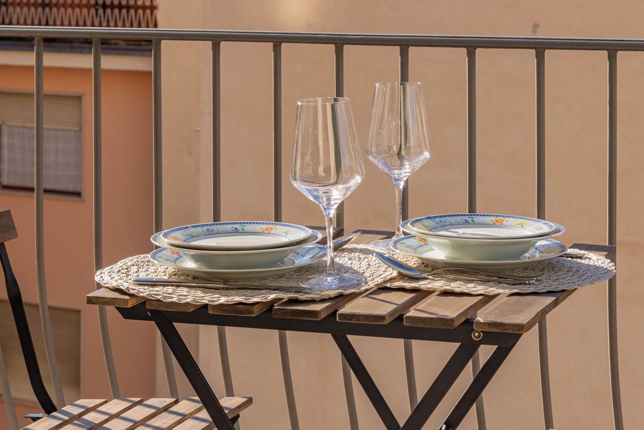 A table set with plates and two wine glasses on a balcony with a metal railing.