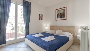 A hotel room with a large bed, a balcony with curtains, a framed picture on the wall, and a radiator. - Casapa - Parking - Sanremo (Sanremo)