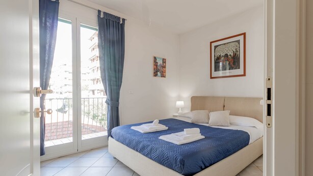 A hotel room with a bed, a balcony, and a view of buildings. - Casapa - Parking - Sanremo (Sanremo)