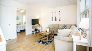 Een woonkamer met een houten salontafel, een beige bank, een televisie en decoratieve items aan de muur.