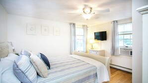 Een slaapkamer met een bed, een plafondventilator, een televisie en een raam met gordijnen.