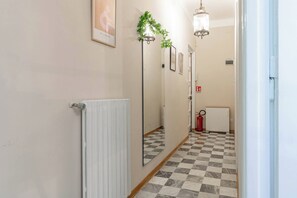 Un couloir avec un radiateur, un sol à carreaux, un extincteur et un miroir qui reflète le couloir.