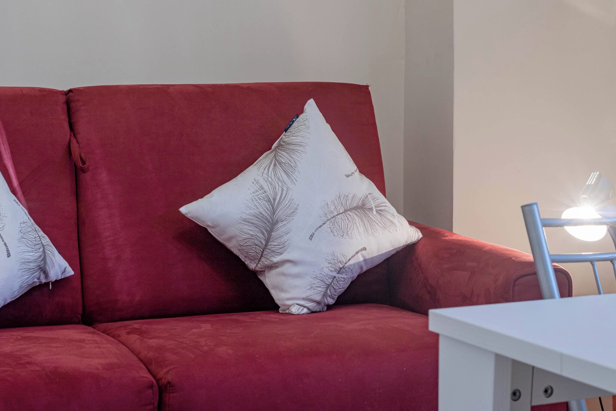 Un canapé rouge avec un coussin blanc orné d’un motif de plumes.
