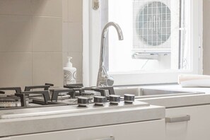 A kitchen with a gas stove, a sink, and a window with a fan.