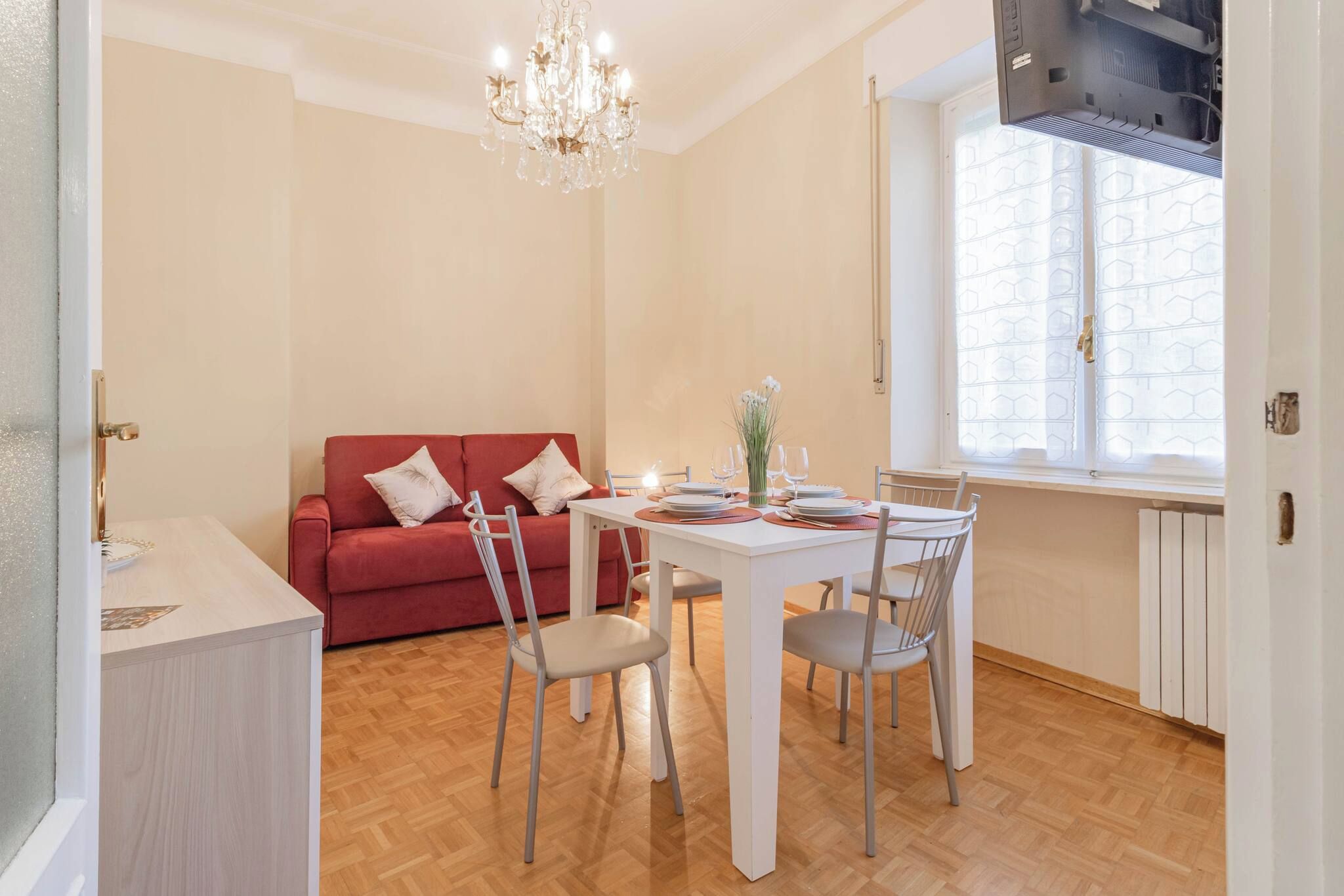 Un coin repas avec une table blanche dressée pour quatre personnes, un canapé rouge et un lustre.