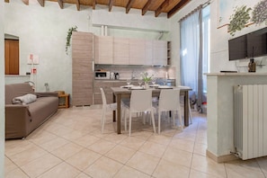 A modern kitchen with a dining area, a sofa, and a TV mounted on the wall. - IL NIDO - Centro - Ariston (Sanremo)
