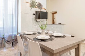 A dining area with a table set for four, a television mounted on the wall, and a kitchen area in the background. - IL NIDO - Centro - Ariston (Sanremo)