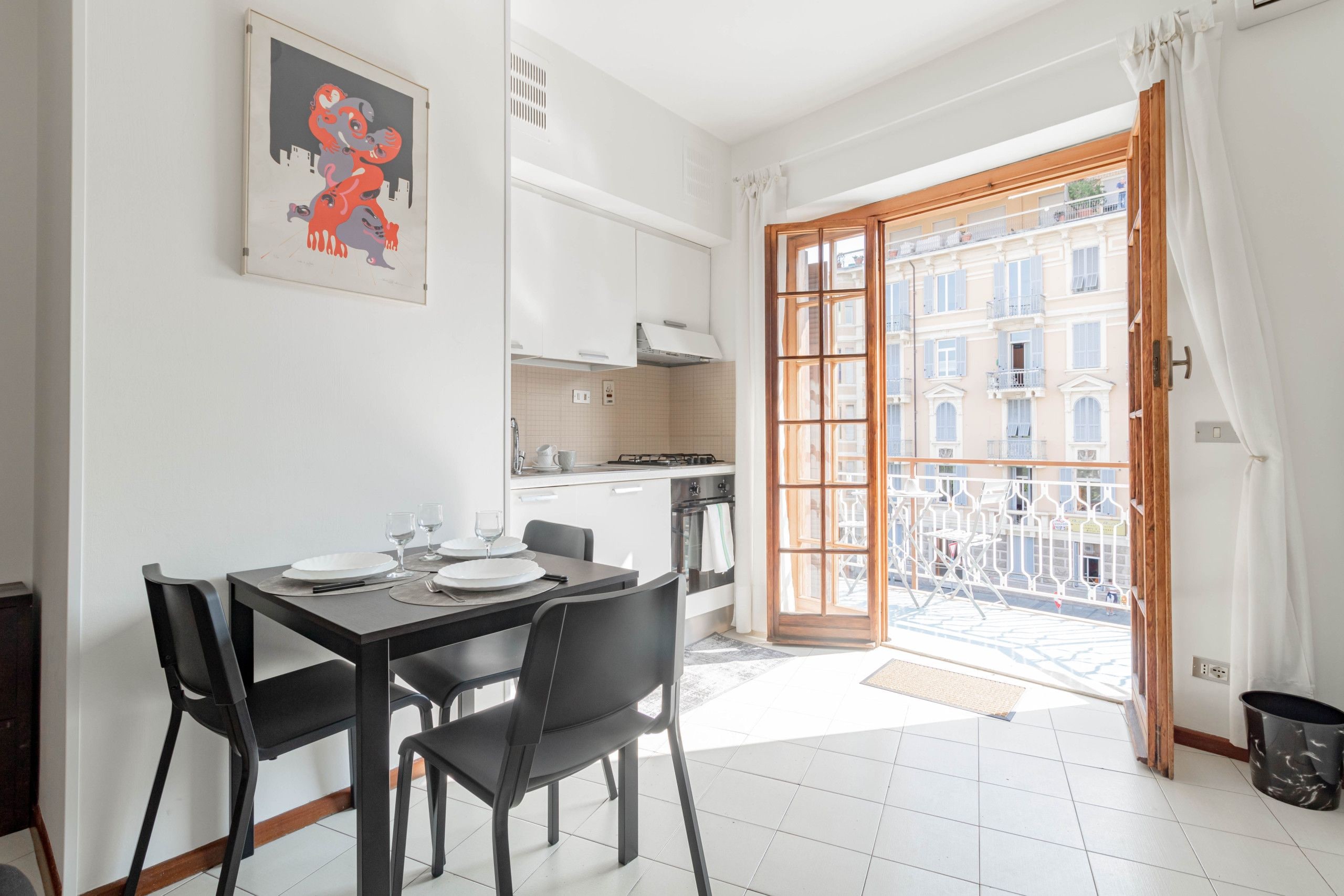 A modern kitchen with white cabinets, a dining table with chairs, and a view of a building through a glass door.