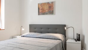 Een slaapkamer met een bed, twee bedlampen, een televisie en een schilderij aan de muur.