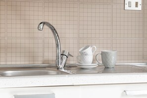 A kitchen sink with a modern faucet, a white coffee cup, and a matching saucer on the countertop.