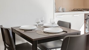 Een eettafel gedekt met borden, glazen en bestek, met stoelen eromheen.