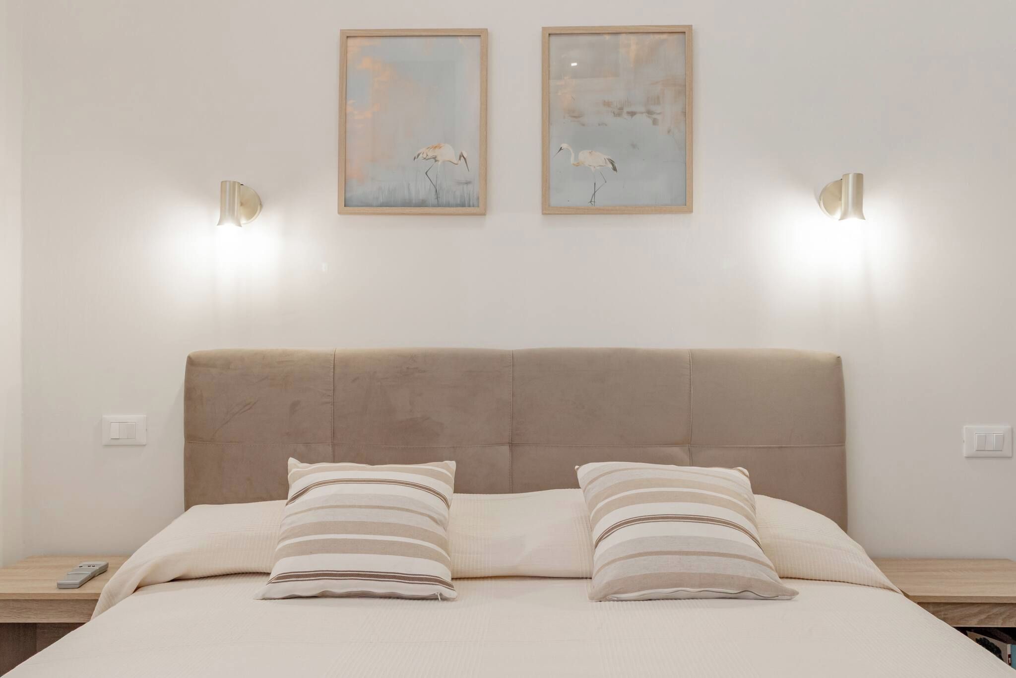 A bed with a headboard, two bedside lamps, and two framed artworks above.