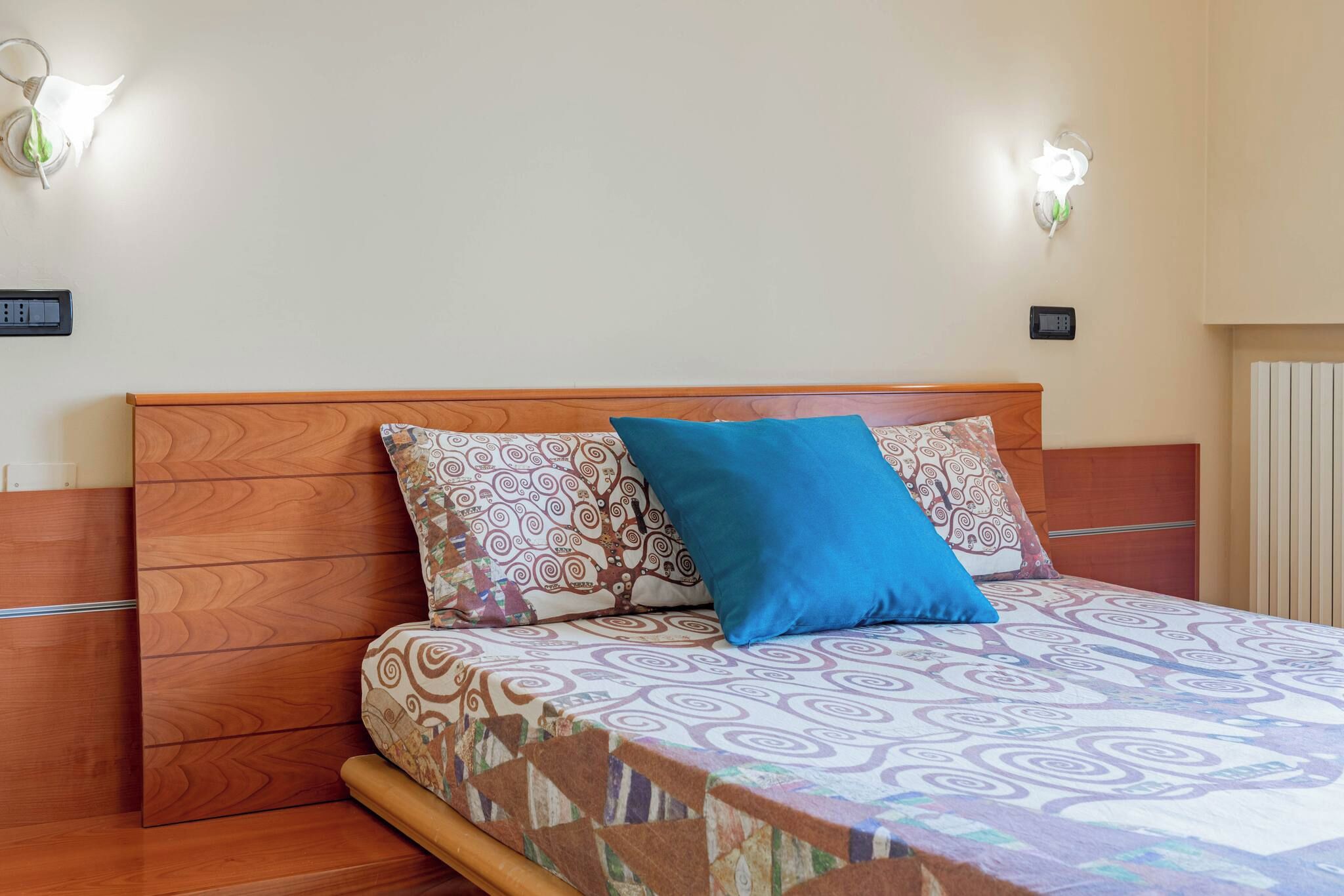 A bed with patterned bedding, a blue pillow, and two wall-mounted light fixtures.