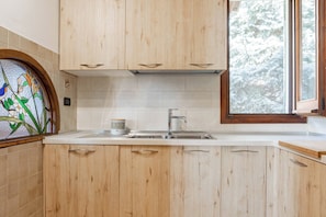 A kitchen with wooden cabinets, a stainless steel sink, and a window with a view of snow-covered trees.