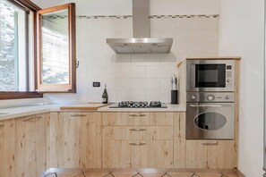 A modern kitchen with wooden cabinets, a gas stove, a built-in oven, and a microwave. - OASI SERENA - Parcheggio-Giardino (Liguria)