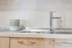 Una cocina con un lavamanos de acero inoxidable, un mueble de madera con un tirador y un recipiente colorido sobre la encimera.