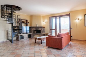 A living room with a fireplace, a sofa, a TV, and a spiral staircase. - OASI SERENA - Parcheggio-Giardino (Liguria)