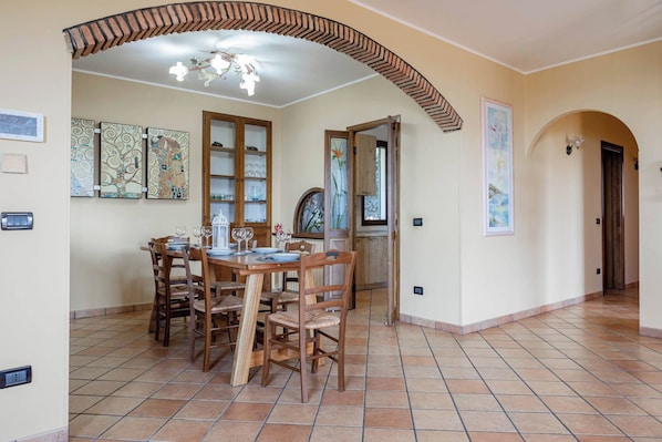 A dining area with a wooden table and chairs, a chandelier, and a tiled floor.