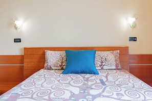 Una cama con colcha estampada, dos almohadas, cabecera de madera y apliques de luz en la pared.