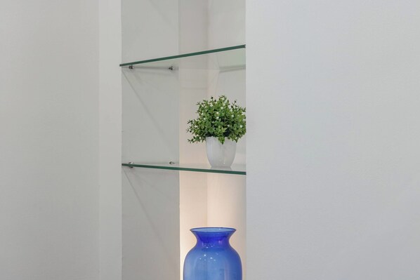 A glass shelf with a white vase containing a green plant and a blue vase.