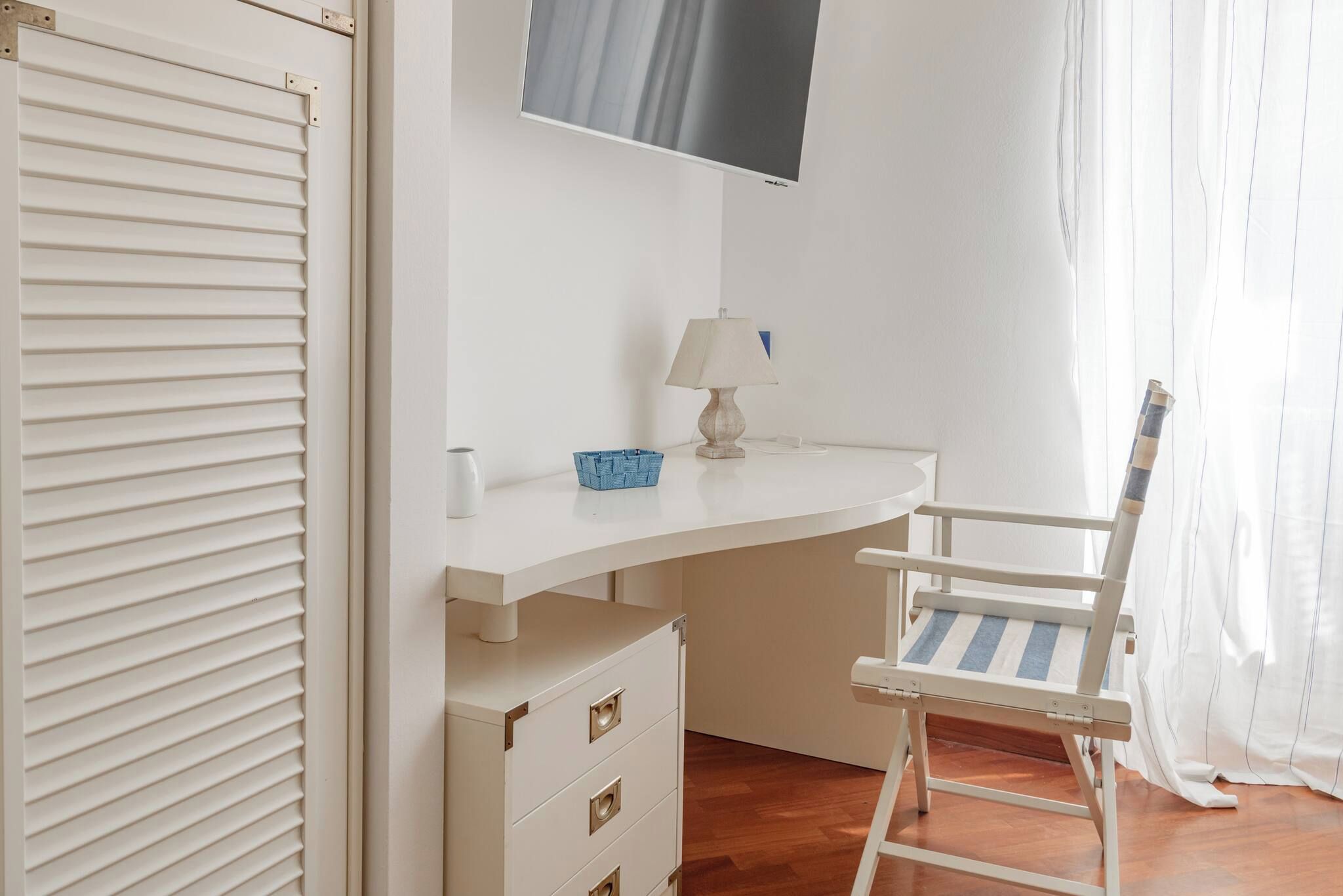 Une pièce avec un bureau blanc, une chaise, une lampe et un téléviseur fixé au mur.