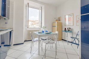 A modern kitchen with a dining table, chairs, a refrigerator, and a window with a view of buildings.