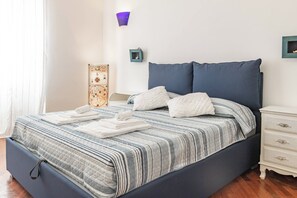A neatly made bed with a striped bedspread and pillows, a bedside table with a lamp, and a decorative item on the wall.