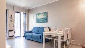 A modern living room with a blue sofa, a white dining table, and a painting of a seascape. - Silver House in Sanremo (Sanremo)