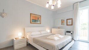 A modern bedroom with a large bed, bedside tables, a ceiling light, a wall-mounted air conditioner, and a window with curtains. - Silver House in Sanremo (Sanremo)
