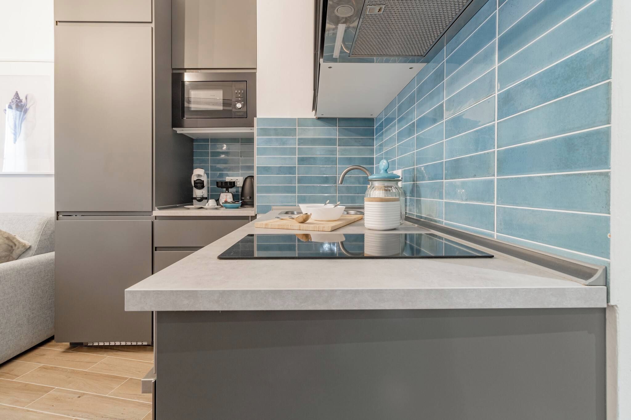 Une cuisine moderne dotée d’un îlot central intégré, de meubles de couleur grise et d’un dosseret de carreaux bleus.