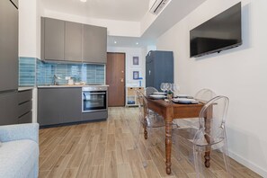 A modern kitchen with grey cabinets, a built-in oven, and a dining area with a wooden table and clear chairs. - SUITE LA MER - Sanremo - Spiagge (Sanremo)