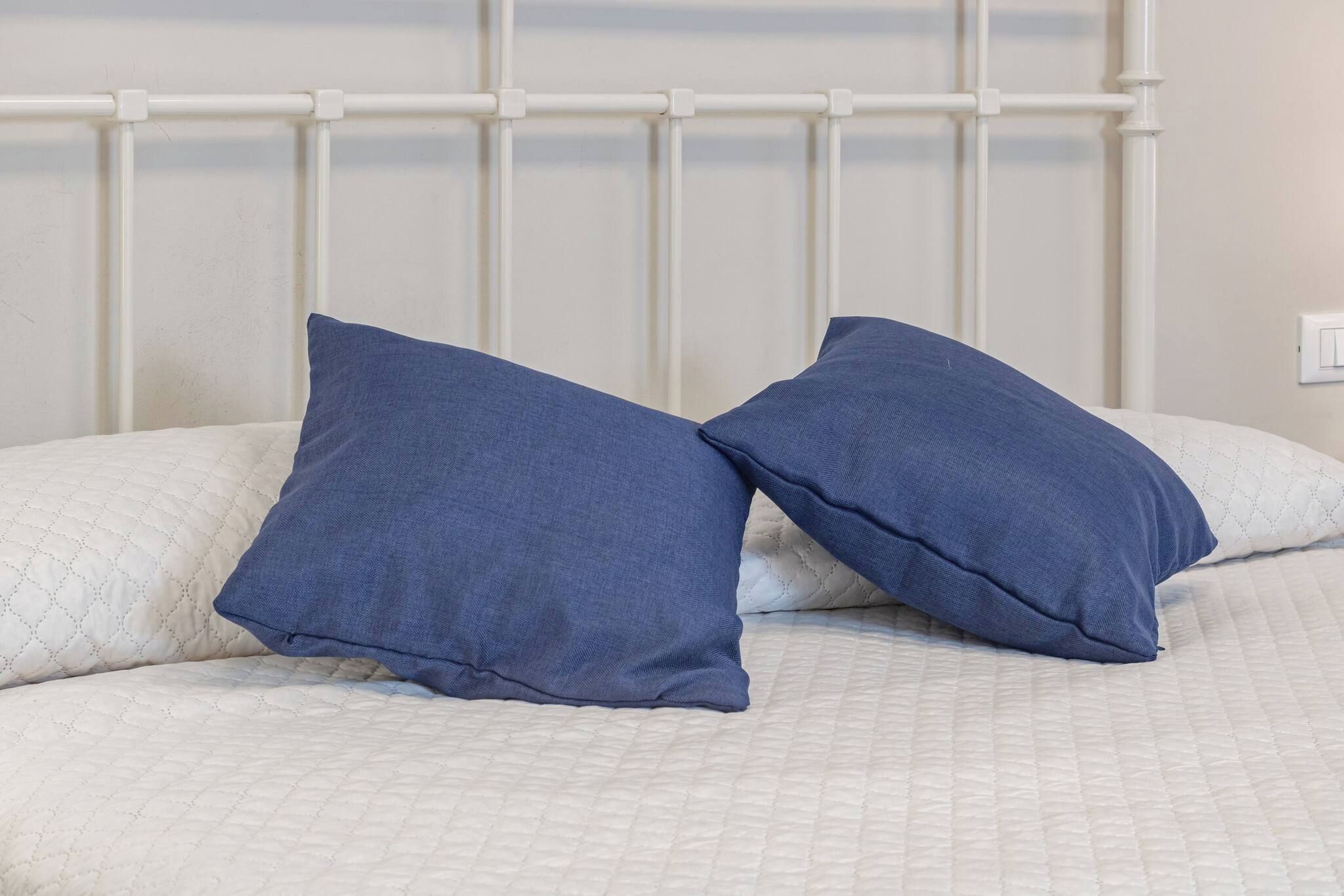 Una cama con cabecera blanca y dos almohadas azules.