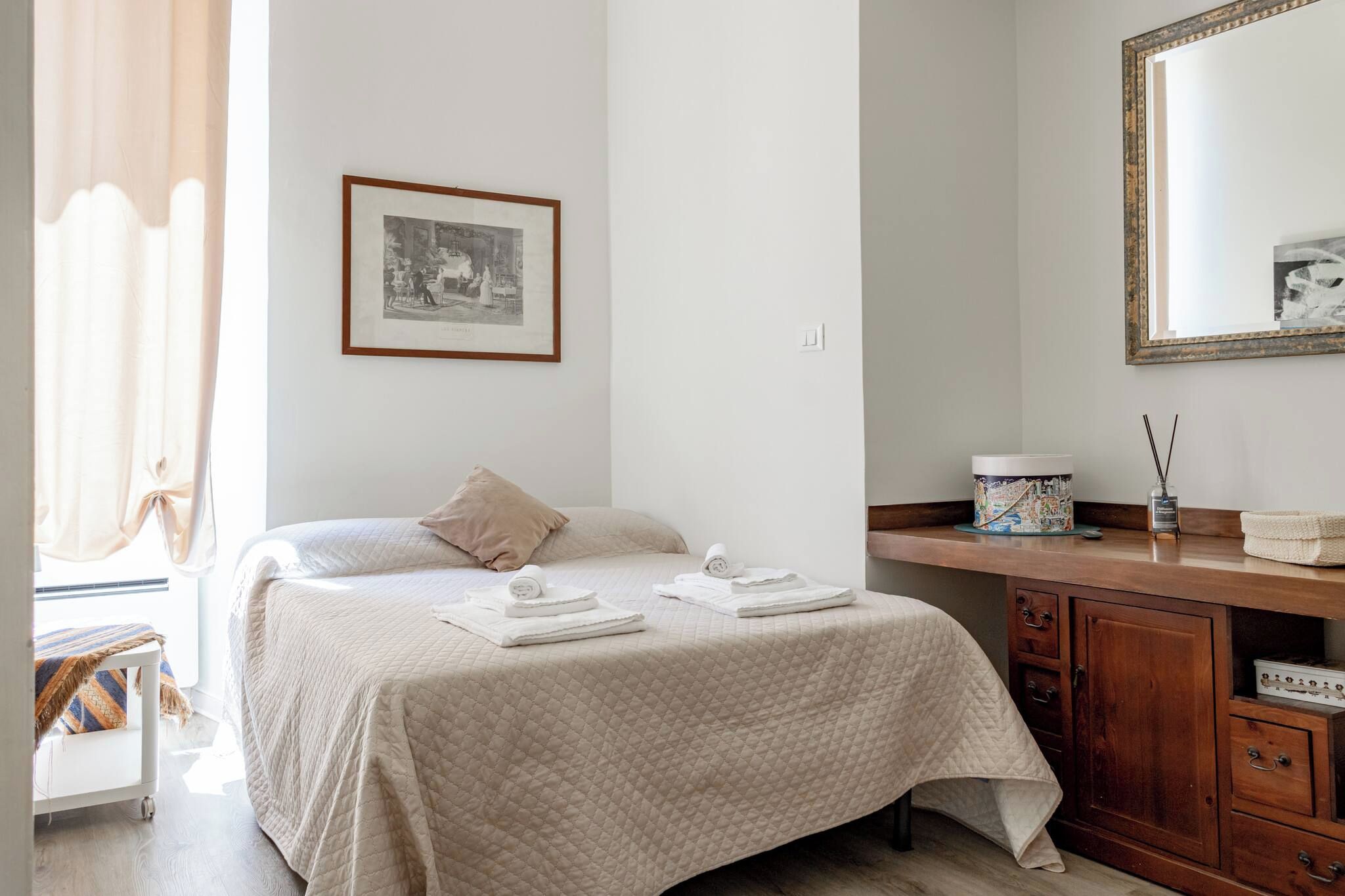 Una habitación de hotel con una cama, una mesita de noche con lámpara, un espejo y un cuadro en la pared.