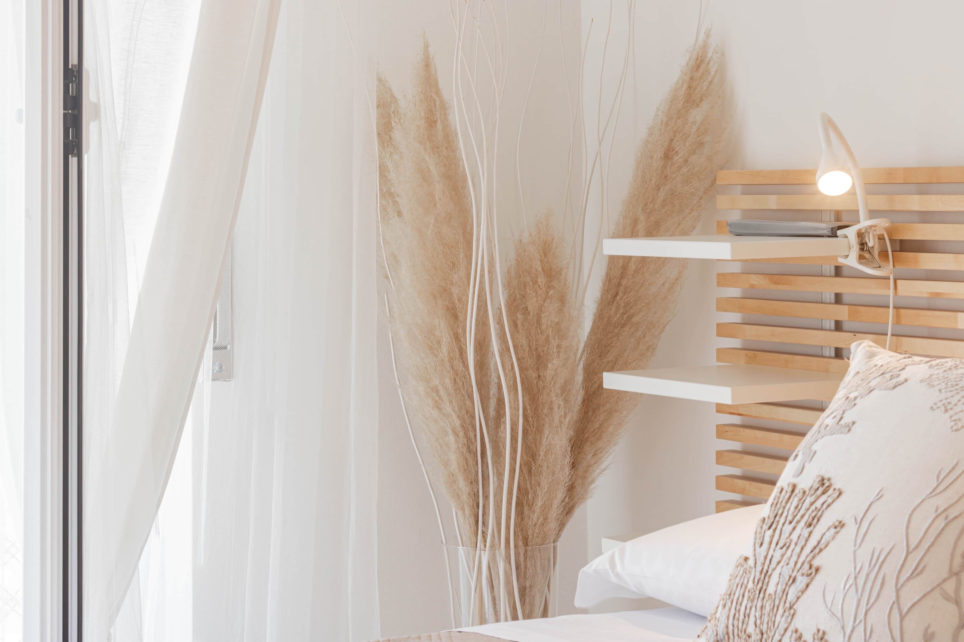 Une chambre à coucher avec un lit, une table de chevet, une lampe et une fenêtre avec des rideaux légers.