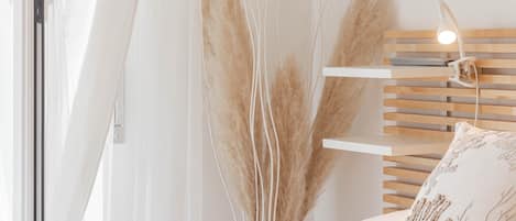 Une chambre à coucher avec un lit, une table de chevet, une lampe et une fenêtre avec des rideaux légers.
