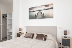 Een slaapkamer met een bed, twee nachtkastjes, een kledingkast en een schilderij van een pier aan de muur.