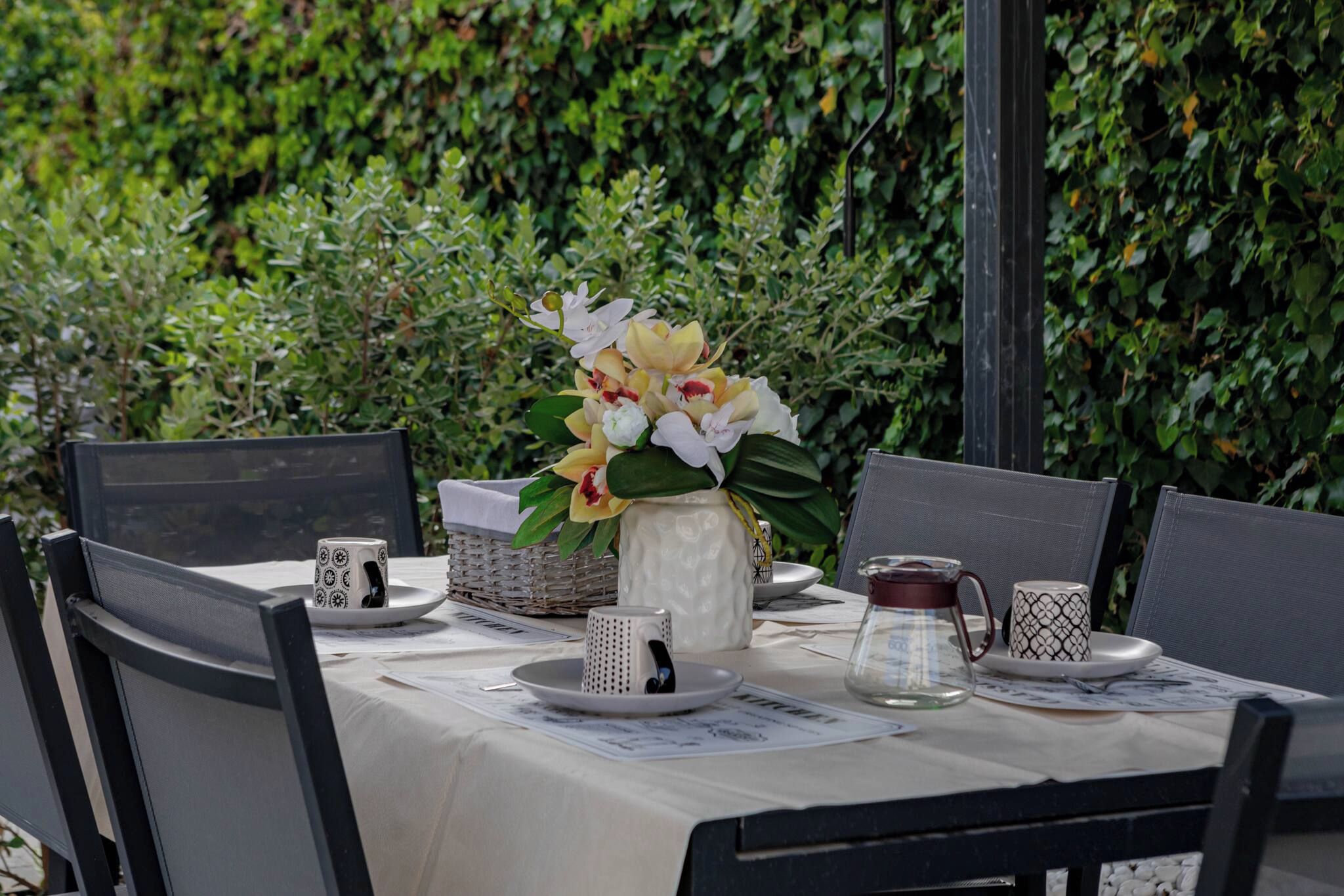 A table set outdoors with a vase of flowers, a coffee pot, and various tableware.