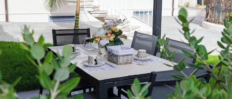An outdoor dining area with a table set for two, surrounded by greenery.