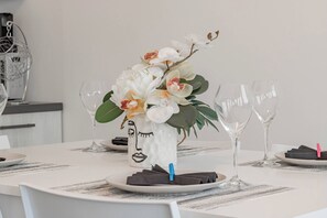 A dining table set with white plates, clear wine glasses, and a centerpiece of white flowers in a vase. - VILLA MIA - Giardino-Parcheggio (Sanremo)