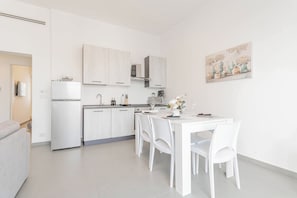 Een moderne keuken met witte kastjes, een eettafel met stoelen en een schilderij aan de muur.